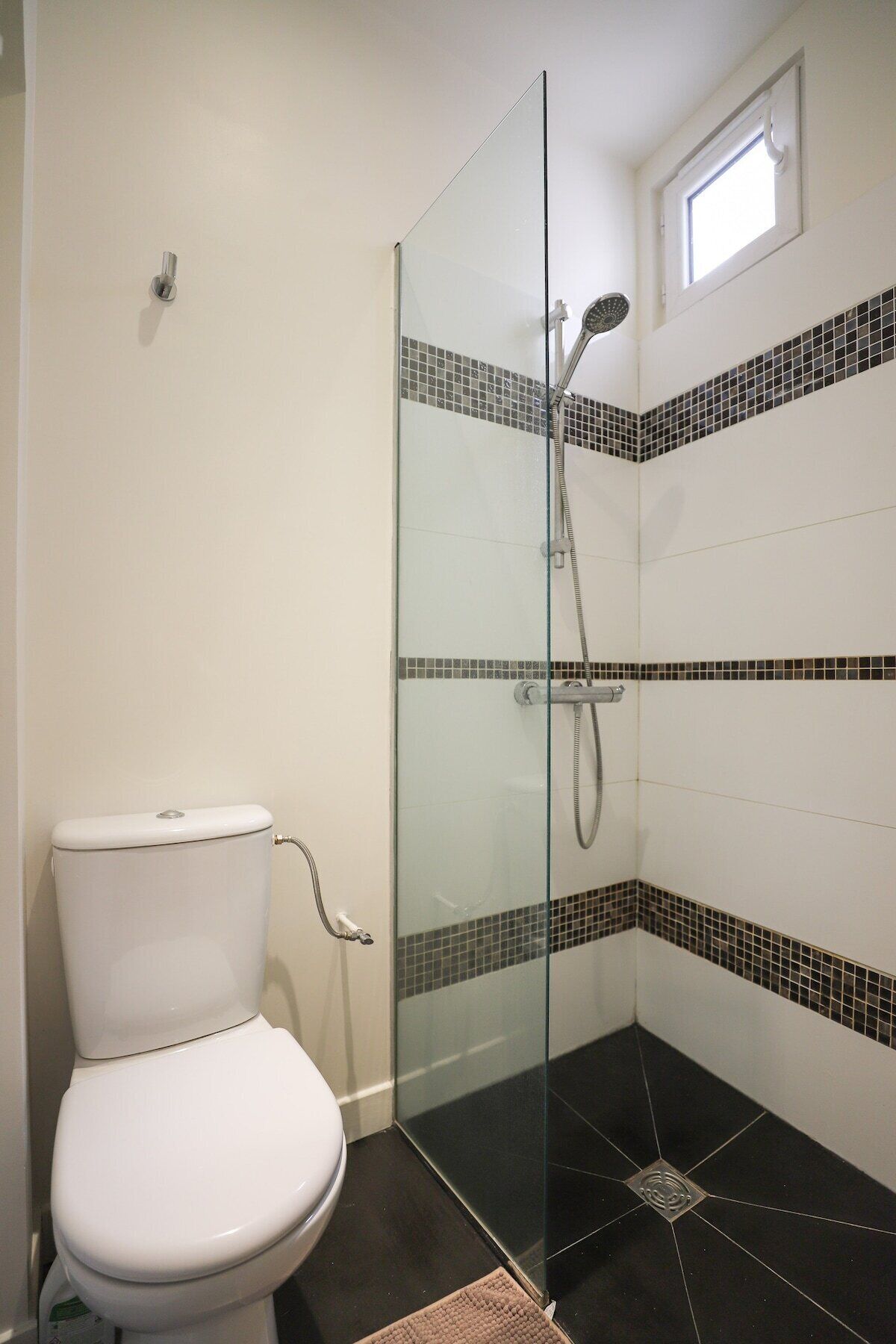Ein Badezimmer mit einer Glaskabinentrennwand, einer weißen Toilette und schwarz-weißen Fliesen.
