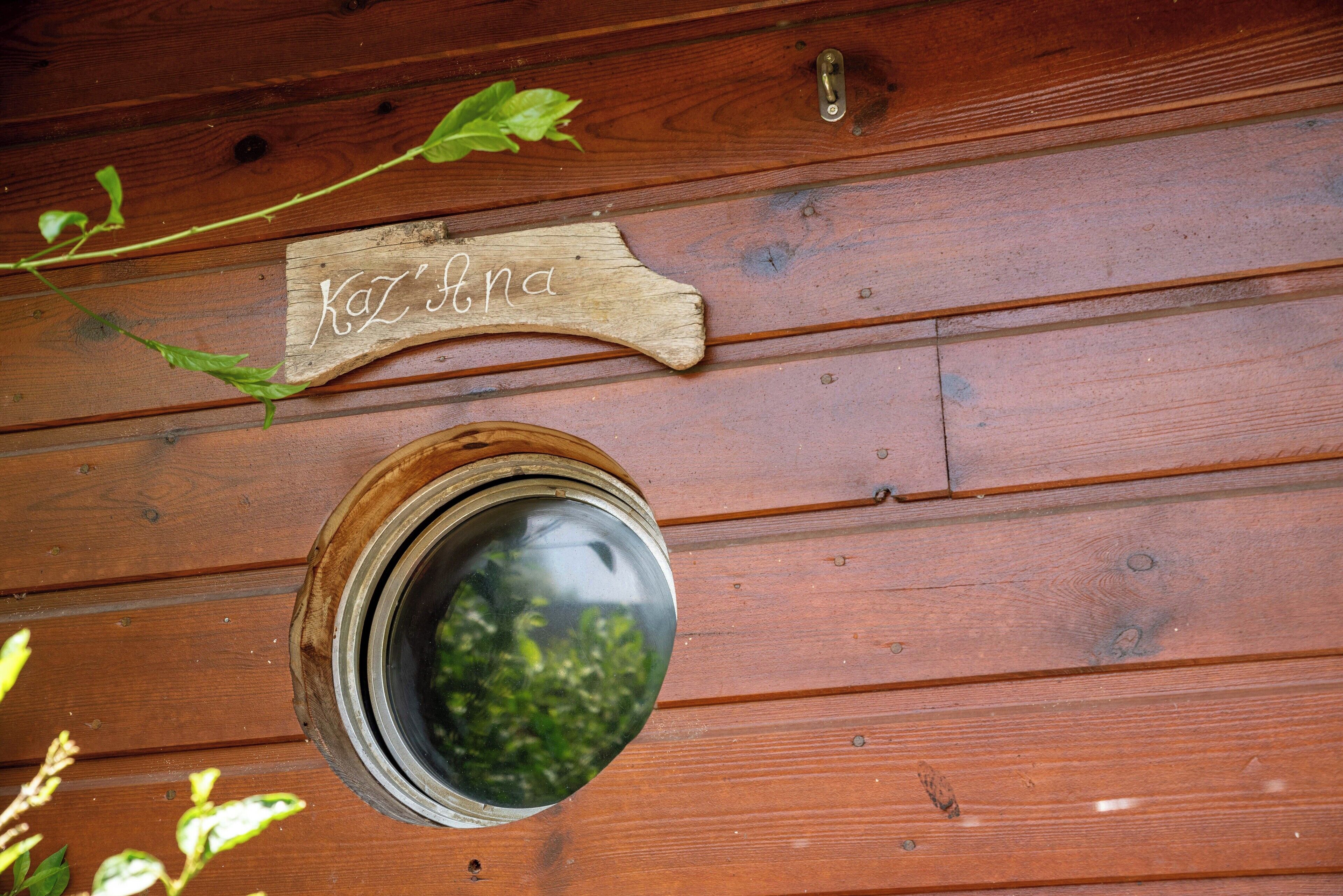 Un mur en bois sur lequel est fixée une plaque avec le nom « KAZ’ANA » et un miroir rond.