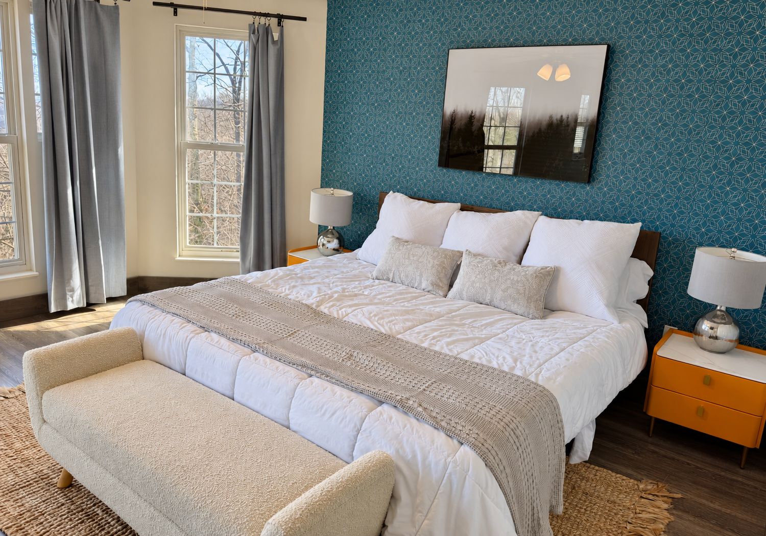 Une chambre à coucher avec un grand lit, deux tables de chevet, un banc, une fenêtre avec des rideaux et une œuvre d’art accrochée au mur.