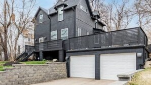 A two-story house with a garage, a staircase leading to the second floor, and a stone retaining wall. - Gorgeous Midtown 3 Bedroom Home (Omaha)