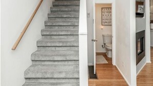 A staircase with a wooden handrail leading to a room with a toilet and a framed sign on the wall. - Gorgeous Midtown 3 Bedroom Home (Omaha)