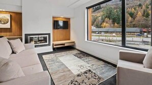 Una sala de estar moderna con un sofá, una chimenea, un televisor y un ventanal con vistas a un paisaje montañoso.