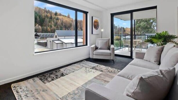 Una sala de estar moderna con un ventanal grande, un sofá, un sillón y una alfombra.