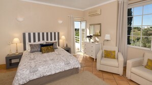 Un dormitorio con cama, mesitas de noche, cómoda, una silla y ventana con vistas.