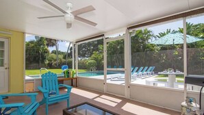 A sunroom with a view of a swimming pool, a ceiling fan, and blue Adirondack chairs.