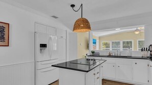 A modern kitchen with white cabinetry, a black countertop island, and a woven pendant light.