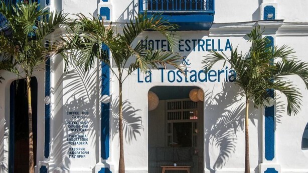 A building with a sign reading "HOTEL ESTRELLA & La Tostaderia," featuring a white facade with blue accents and potted palm trees in front. - Hotel Estrella San Juan Del Sur (San Juan del Sur)