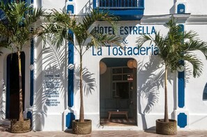 A building with a sign reading "HOTEL ESTRELLA & La Tostaderia," featuring a white facade with blue accents and potted palm trees in front. - Hotel Estrella San Juan Del Sur (San Juan del Sur)