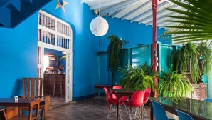 A dining area with red and blue chairs, a wooden table, and a glass table. There are plants and a ceiling fan. - Hotel Estrella San Juan Del Sur (San Juan del Sur)