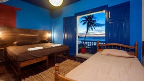 A bedroom with a wooden bed, a nightstand, and a large window with an open door revealing a beach view. - Hotel Estrella San Juan Del Sur (San Juan del Sur)