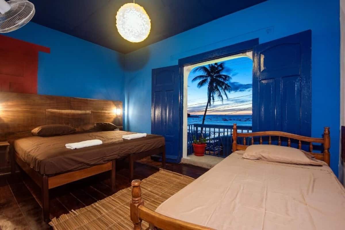 A bedroom with a wooden bed, a nightstand, and a large window with an open door revealing a beach view.