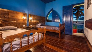 A room with a wooden bed, a small table, a nightstand, and a window with a view of a palm tree. - Hotel Estrella San Juan Del Sur (San Juan del Sur)
