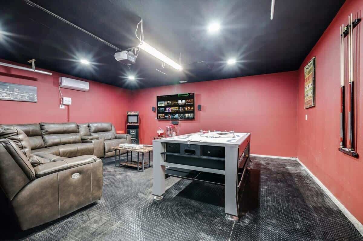 Une pièce avec un mur rouge, un canapé en cuir marron, une table de billard et un écran de projection.