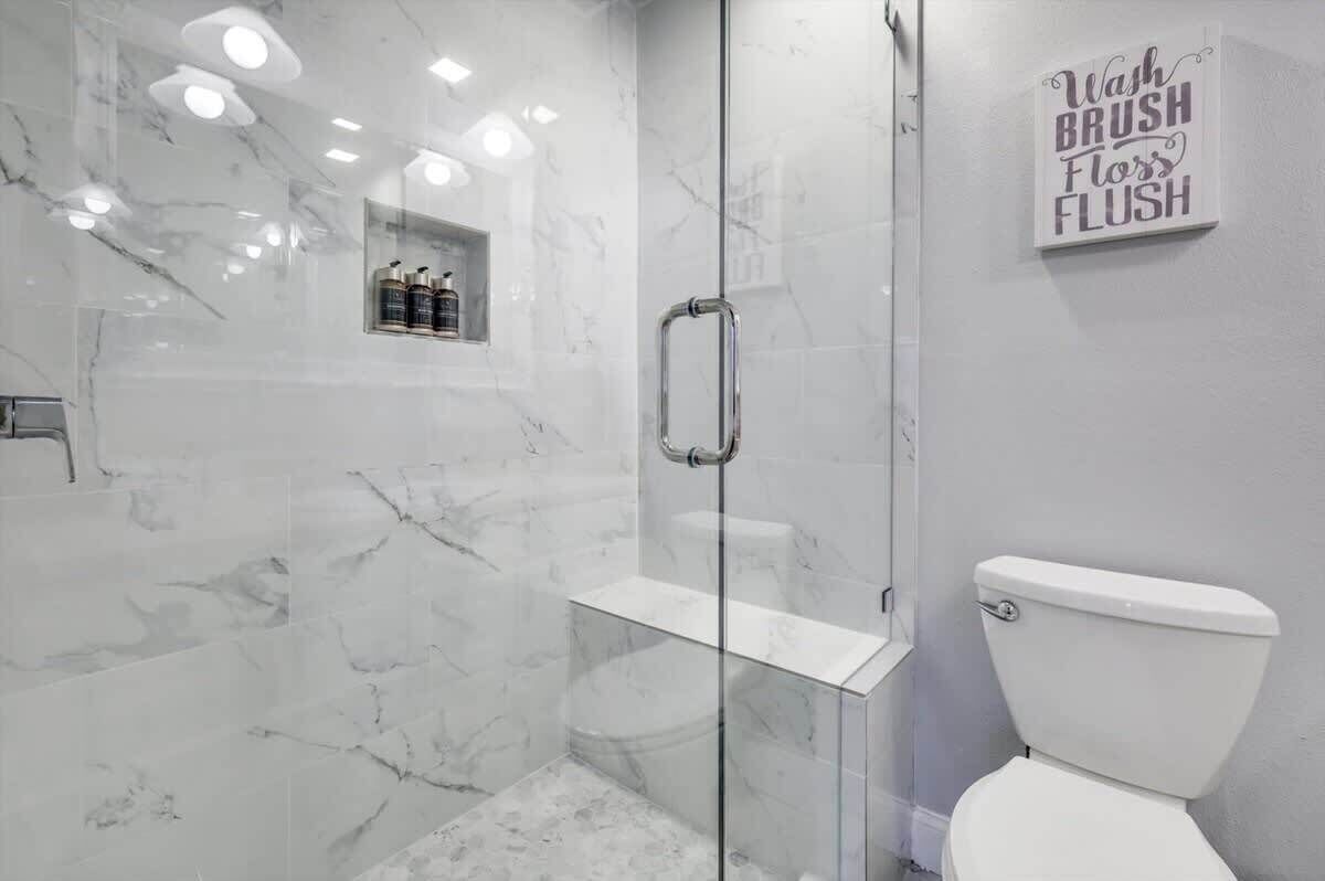 Une salle de bain moderne avec une douche à parois de verre, des toilettes et une étagère contenant des articles de toilette.
