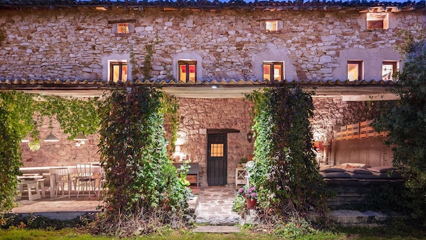 Un edificio de piedra con un patio cubierto, mesas al aire libre y una puerta que da al interior.