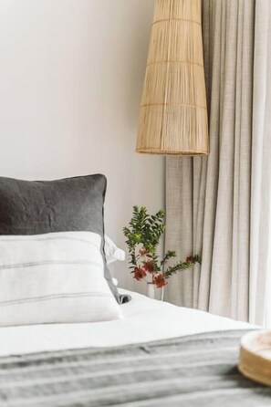 A neatly made bed with a grey and white pillow, a bamboo lamp, and a plant beside a window with curtains.