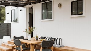 Um pátio externo com mesa e cadeiras de madeira, um banco e um vaso com planta.