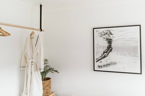 A bathroom with a white bathtub, a wooden towel rack, a framed black and white photograph on the wall, and a potted plant.