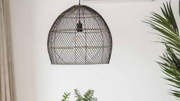 A round wooden dining table with wicker chairs, a black metal pendant light, and a small potted plant.