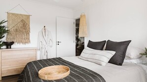 Quarto com cama, mesa de cabeceira, luminária pendente e um objeto decorativo na parede.
