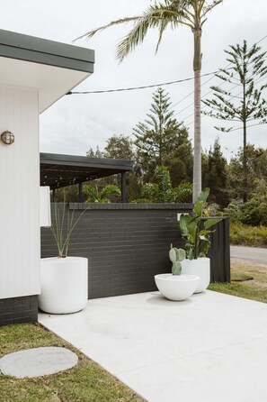 Zona exterior moderna amb un edifici blanc, una tanca negra i grans planters amb vegetació.