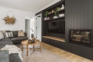A modern living room with a dark wall, a fireplace, a sofa, a coffee table, and a television. - The Lull Culburra (Culburra Beach)