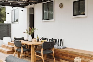 An outdoor patio with a wooden table and chairs, a bench, and a potted plant.