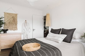 A bedroom with a bed, a bedside table, a hanging light fixture, and a wall hanging. - The Lull Culburra (Culburra Beach)