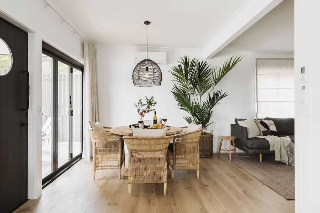 A dining area with a round table, wicker chairs, and a hanging light fixture.