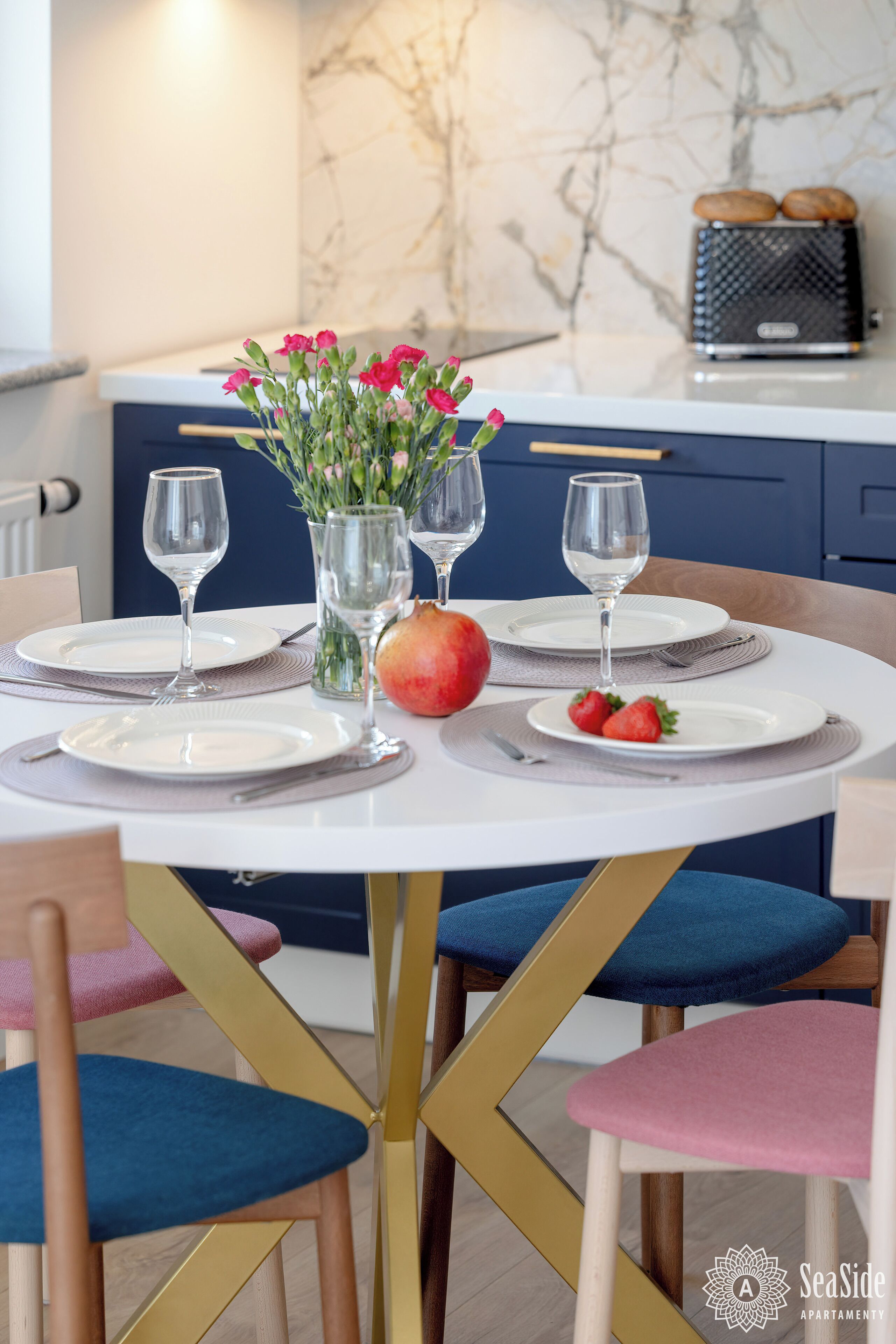 Una mesa de comedor dispuesta con platos, cubiertos y vasos, un florero con flores y una granada sobre la mesa.