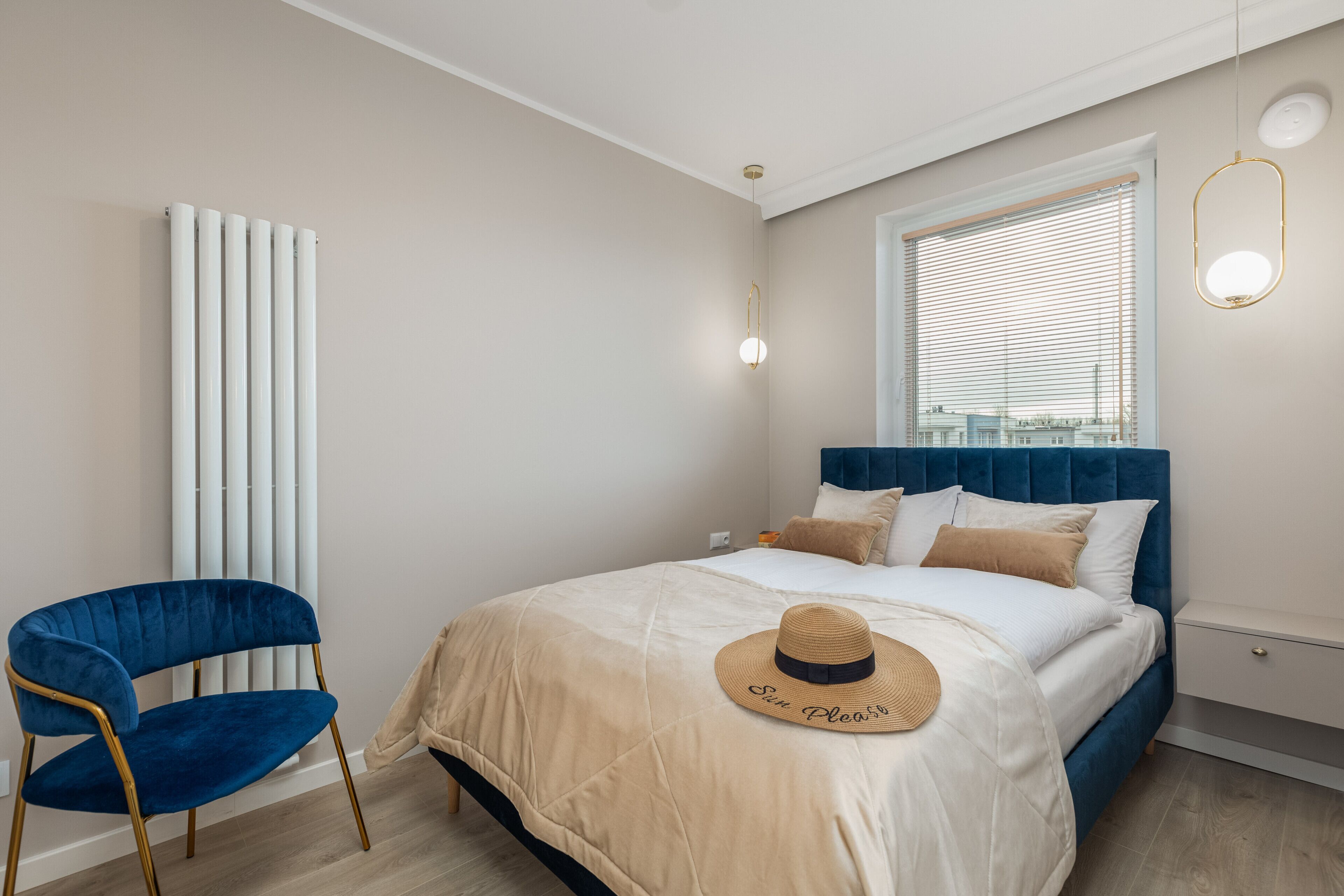 Un dormitorio con una cama, una silla azul, un radiador y una ventana con persianas.