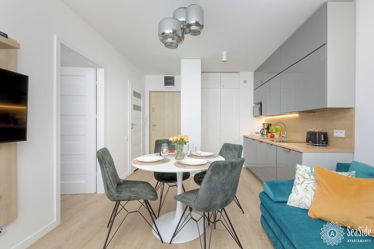 A modern kitchen with white cabinets, a dining table with chairs, and a TV mounted on the wall.
