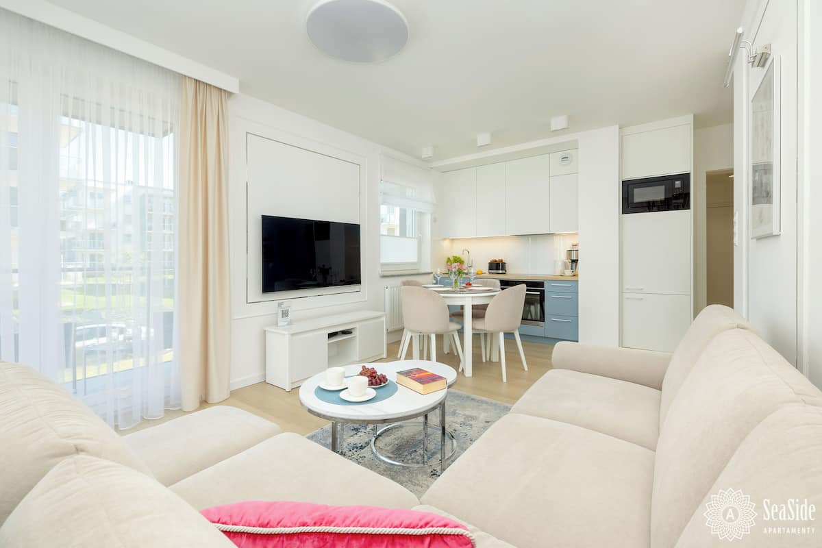 A modern living room with a sofa, a coffee table, and a TV. There is a kitchen area with a dining table and chairs.