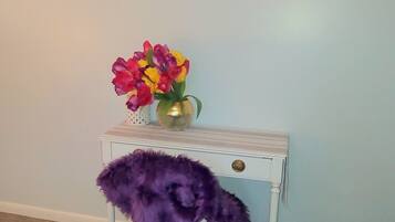 A room with a wall-mounted sign reading "GAIL SUITE" and a small white table with a purple furry chair and a vase of flowers.