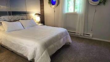 A bedroom with a large bed, a view of the sea through a window, and two wall-mounted lamps with blue lights.