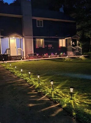 Un bâtiment doté d’un porche abrité, d’une pelouse agrémentée de jeux de lumière décoratifs et d’un chemin.