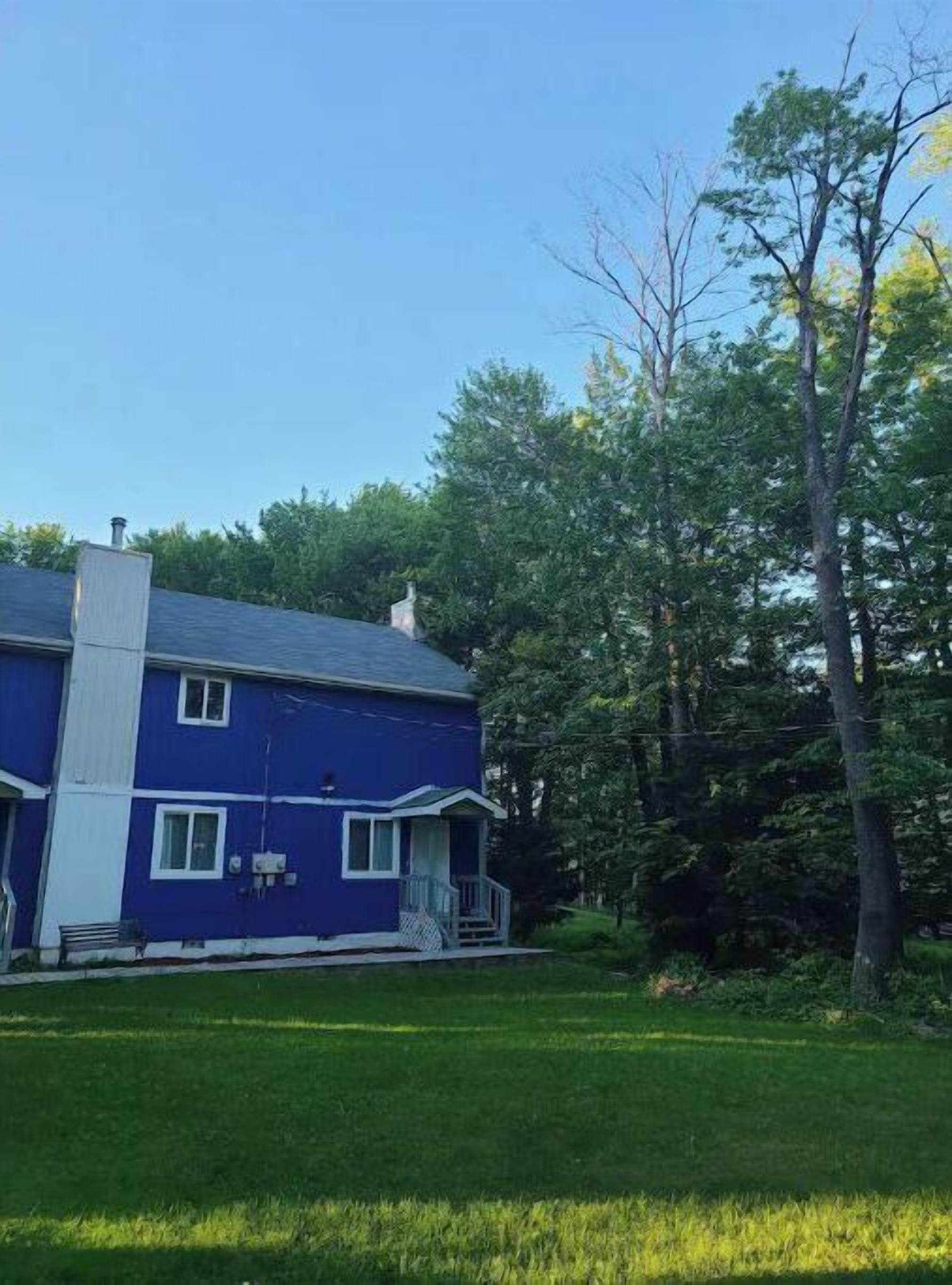 A two-story blue house with a white chimney, a front porch, and a well-maintained lawn.