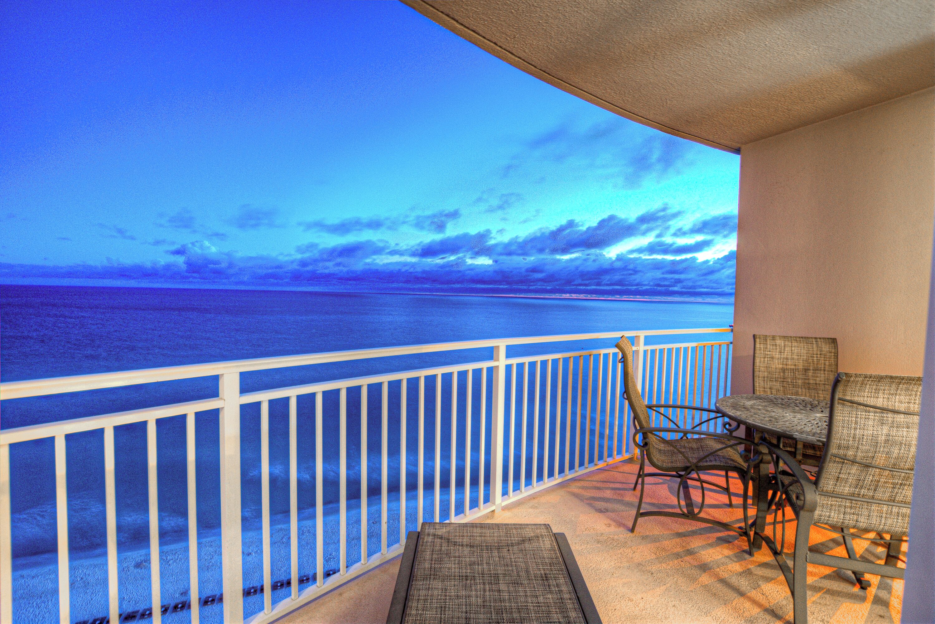 A balcony with a view of the ocean, wicker furniture, and a white railing.