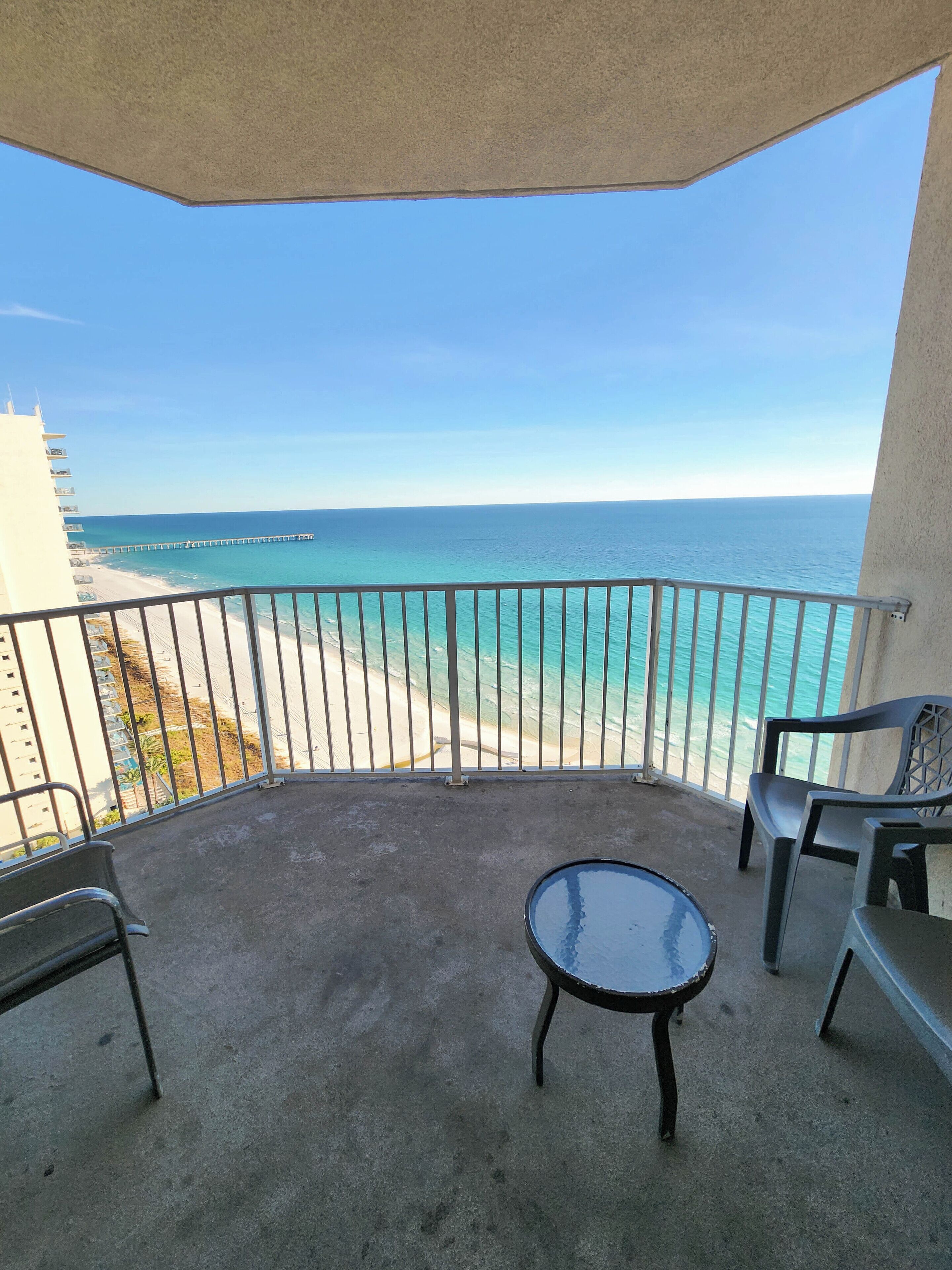 A balcony with a view of the ocean and a pier. There are two chairs and a small table.