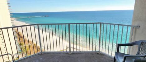 A balcony with a view of the ocean and a pier. There are two chairs and a small table.