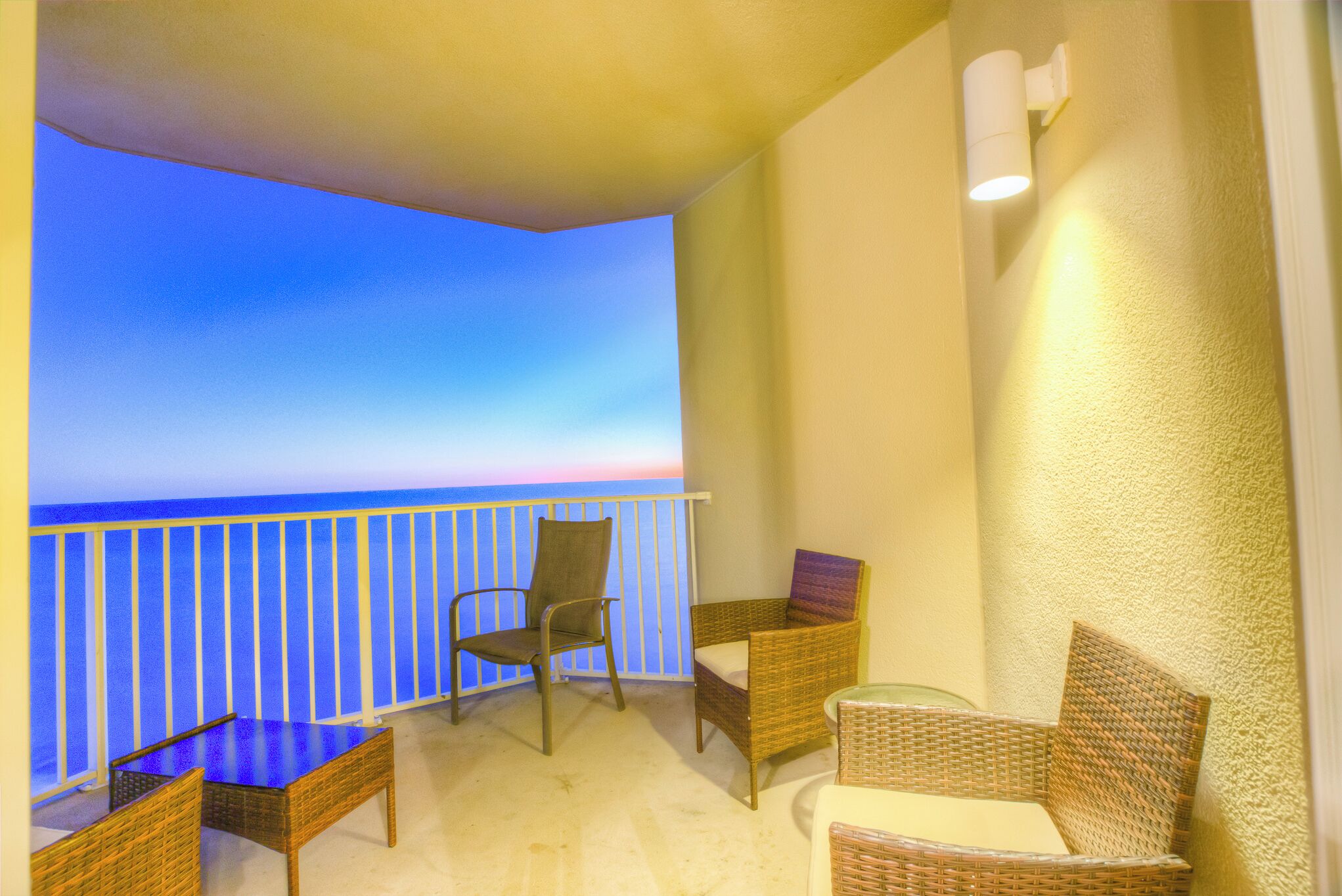 A balcony with wicker furniture, a view of the ocean, and a light fixture on the wall.