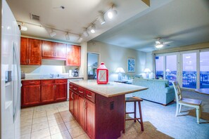 Enjoy cooking in the well-equipped kitchen with a central island and adjacent living area featuring a sofa, dining table, and city view.