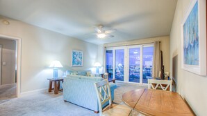 A spacious living room with a large window, a ceiling fan, and a dining area with a wooden table and chairs.