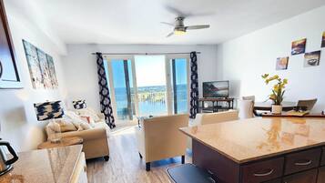 Una cocina moderna con una isla central, un comedor con mesa y sillas, y una sala de estar con sofá y televisor.