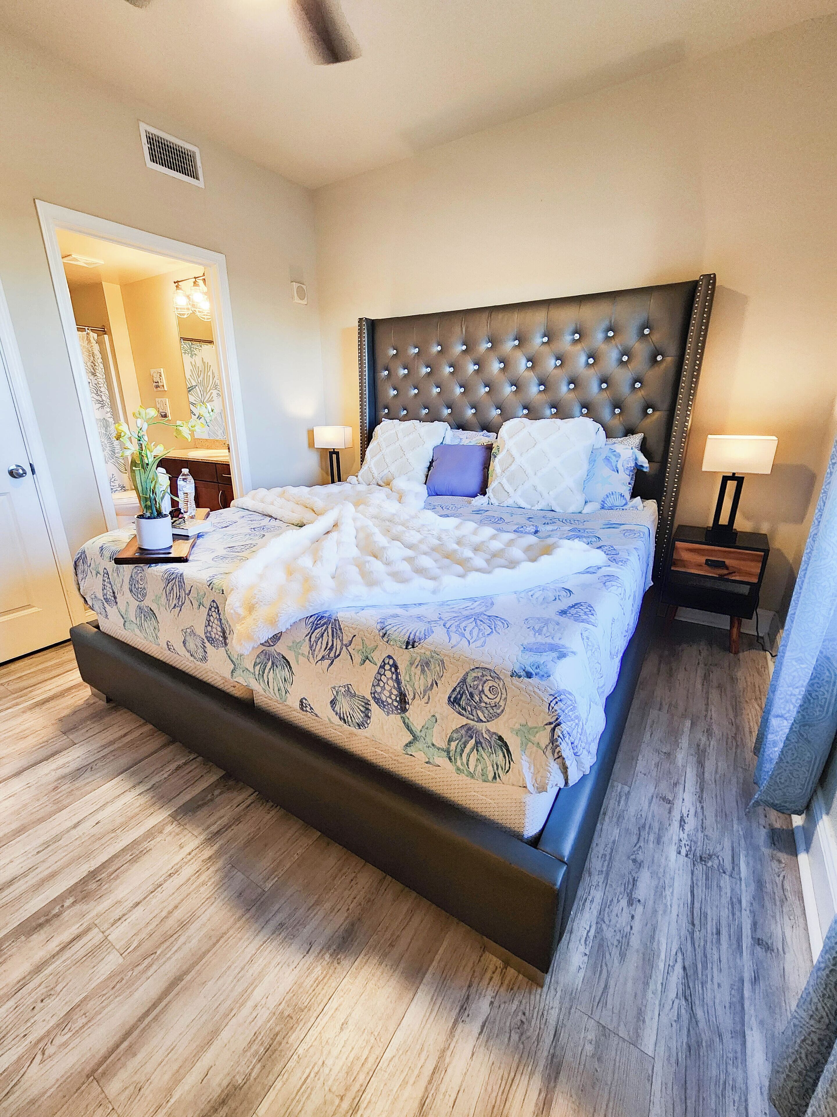 Une chambre spacieuse avec un grand lit, une table de chevet, une commode et une plante en pot.