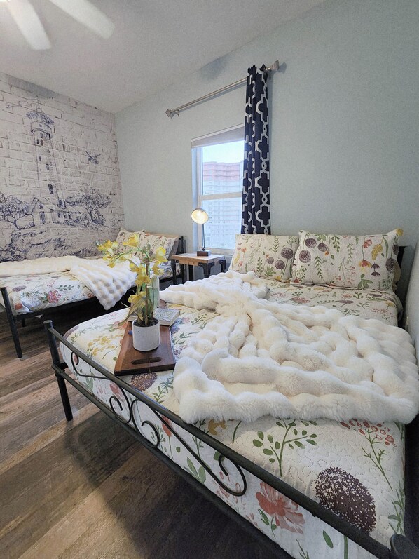 A bedroom with a bed, a nightstand, a lamp, a window with curtains, and a brick-patterned wall.