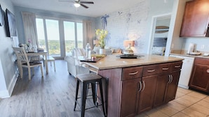 A spacious kitchen with a large island, a dining area with a table and chairs, and a view of the outdoors through large windows. - Private end unit, boasting incredible views for am incredible vacation! (Panama City Beach)