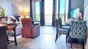 A spacious living area with a wooden floor, a ceiling fan, a sofa, a dining table with chairs, and a balcony with curtains. - On the most private end of the building, accessible and gorgeous! (Panama City Beach)