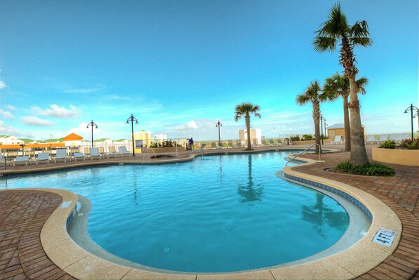 Relax by the serene pool surrounded by palm trees and a brick walkway.