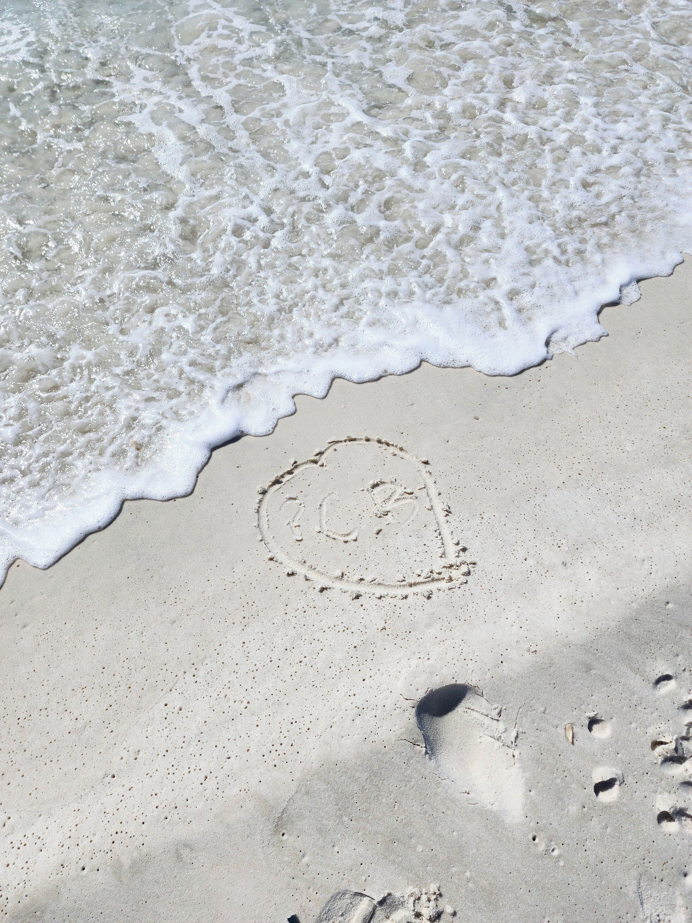 Ein sandiger Strand mit Fußabdrücken und einem herzförmigen Zeichen im Sand.